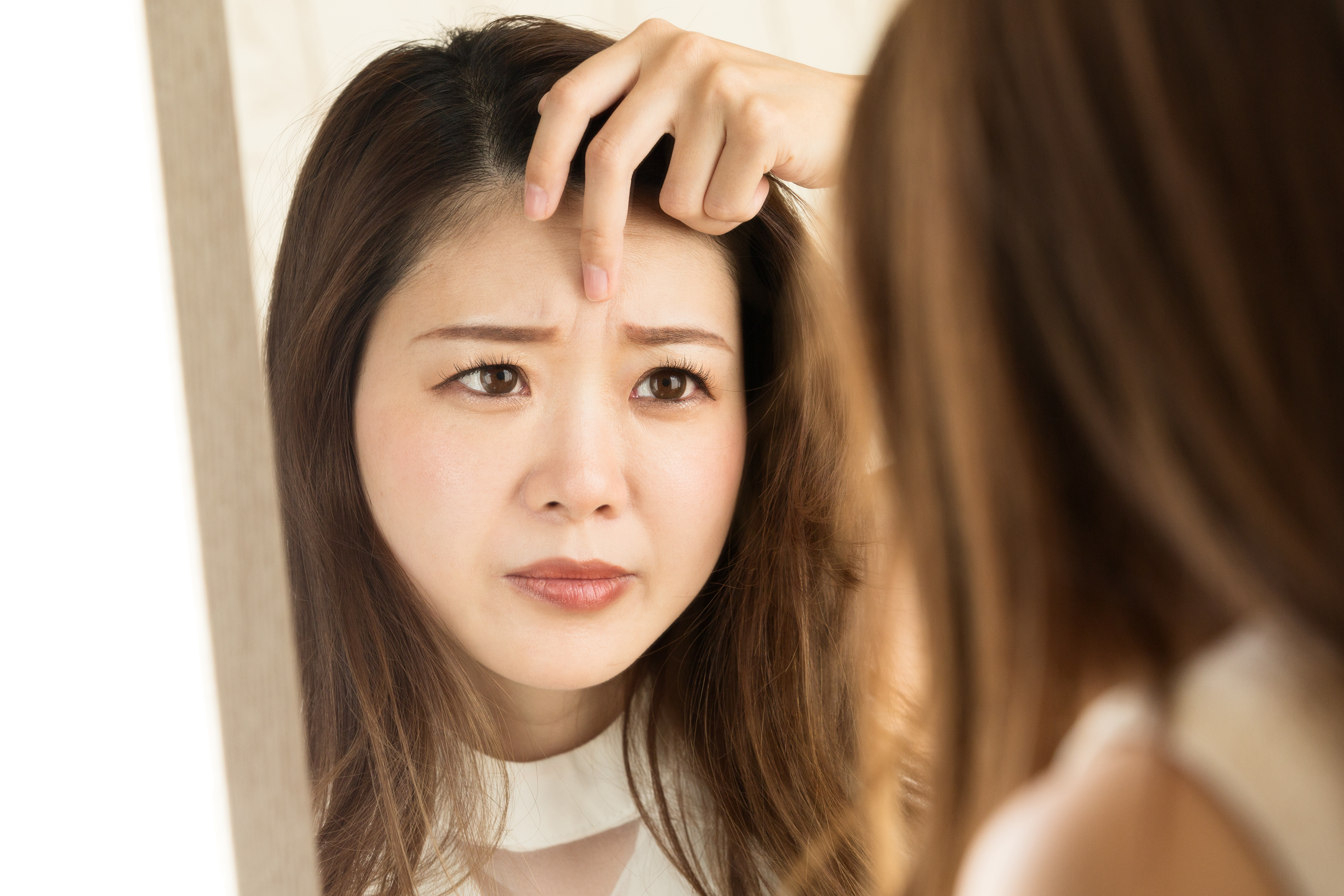 鏡に映る眉間のシワを見る女性